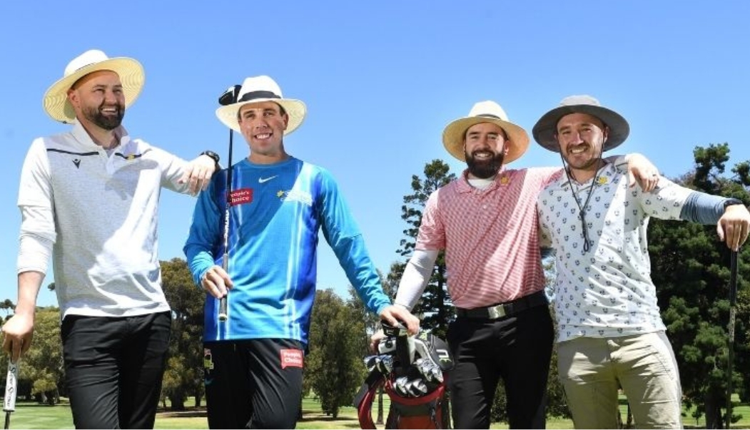 Four men smiling at the camera leaning on their golf clubs