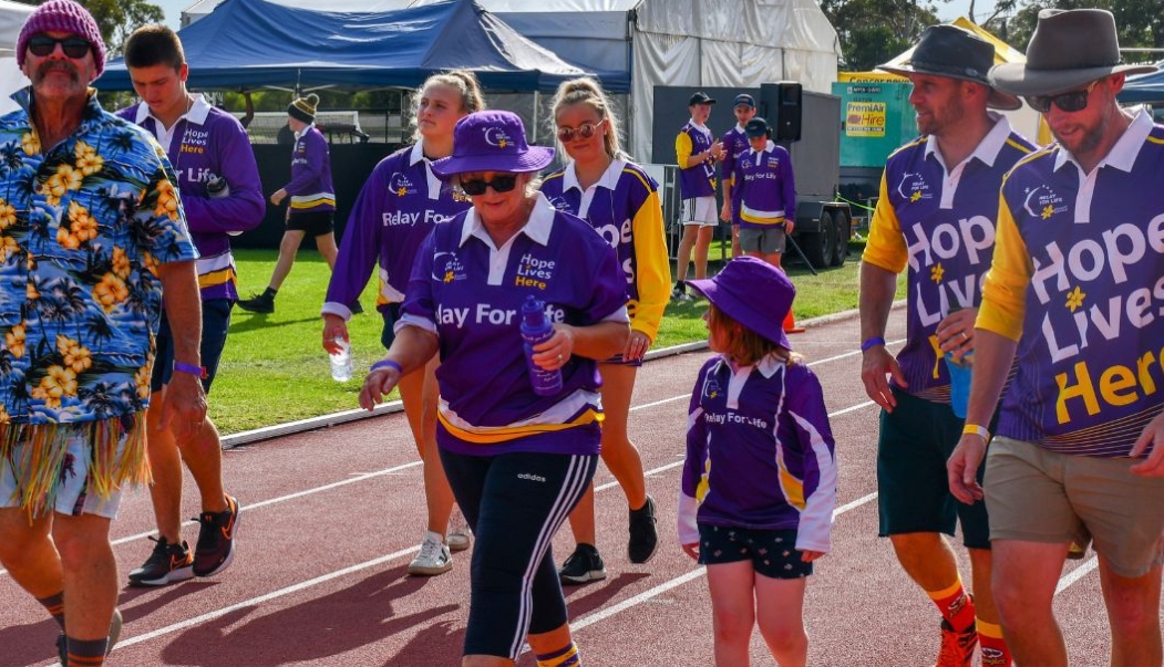 Men Women and children wearing Relay For Life uniforms walking around the track
