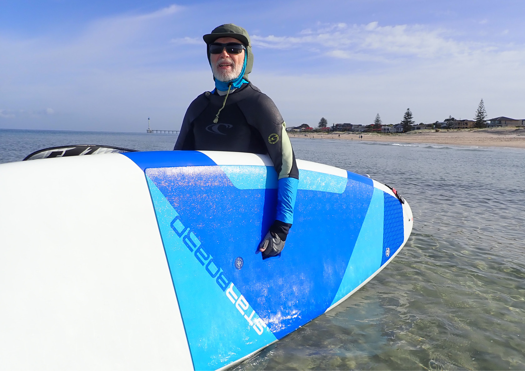 Cancer Connect volunteer Ian holding a surf board at the beach