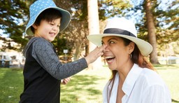 Young child wearing a hat putting sunscreen on smiling mum nose